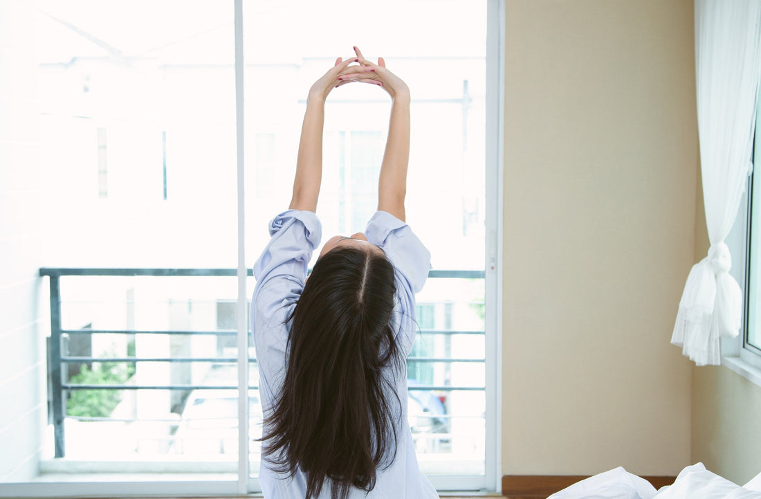 Peaceful young woman waking up at sunrise with light shining through window, symbolizing a reset circadian rhythm