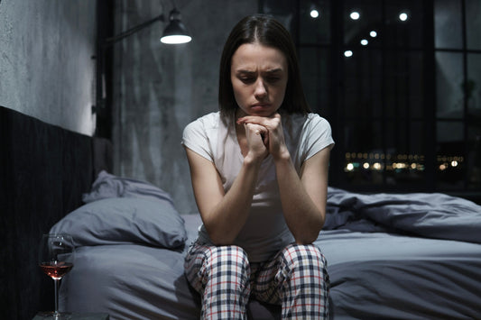 A woman sitting awake in bed at night looking tired and frustrated in dim bedroom lighting